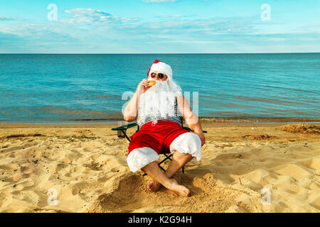 Père Noël sur la plage de manger un hamburger. Le concept d'une mauvaise alimentation. Banque D'Images