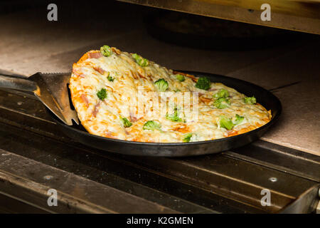 Le chef prend avec une truelle un black metal plaque avec hot pizza fraîchement préparés à partir d'une cuisinière de restaurant ou un café. La Pizza aux légumes Banque D'Images