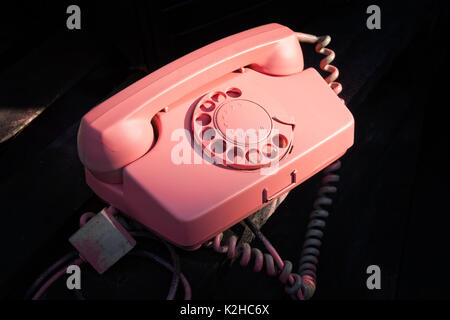 Couleur rose vintage retro éclairée par le téléphone utilisé contre le fond sombre. La technologie de communication du passé. Banque D'Images