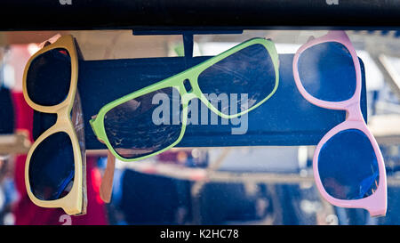 Lunettes colorées de rose, jaune et vert couleurs accrocher sur un rétroviseur derrière le pare-brise d'une voiture. Plus les lunettes de soleil sont pris en compte. Banque D'Images