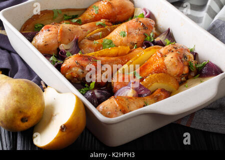 Automne : des aliments cuits au four pilons de poulet avec l'oignon rouge, les poires et les herbes close up dans un plat pour la cuisson. Banque D'Images