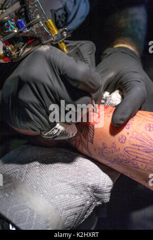 Portant des gants de caoutchouc, un tatoueur dessine une conception sur un avant-bras du client lors d'une convention de tatouage à Costa Mesa, CA. Banque D'Images