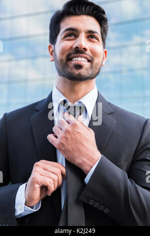 Grave arabe smiling happy businessman positive réussie ou travailleur en costume noir avec barbe, debout devant un immeuble de bureaux et de redresser Banque D'Images