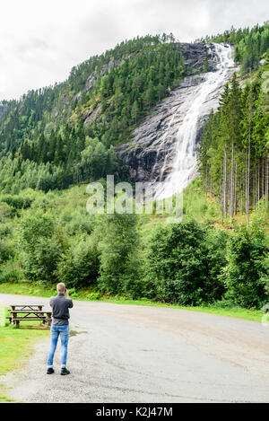 Young adult man standing ci-dessous Woodland Waterfall pour prendre des photos avec votre téléphone mobile. En cascade de l'eau sur la montagne. Dans Reiarsfossen s emplacement Banque D'Images