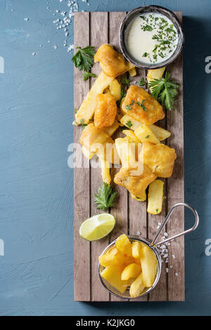 Fast food britannique traditionnel fish and chips. Servi avec sauce au fromage blanc, citron vert, le persil, les frites dans le panier de friture sur sol en bois servant de sélection ove Banque D'Images