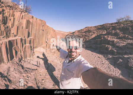 L'homme souriant en tenant à des selfies rocher connu sous le nom de "tuyaux d'orgue" dans le Damaraland, Namibie. Fisheye, la tonalité de l'image. Concept de l'aventure et exp Banque D'Images