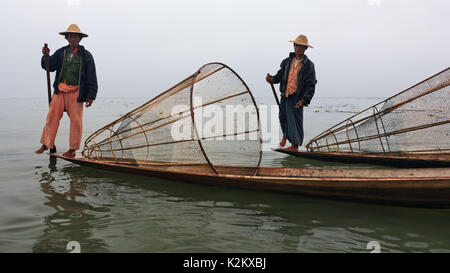 Lac Inle, Myanmar - janvier 04, 2007 : Deux pêcheurs locaux avec des filets de pêche birman debout sur la poupe de longs bateaux à rames et avirons par jambe. Banque D'Images