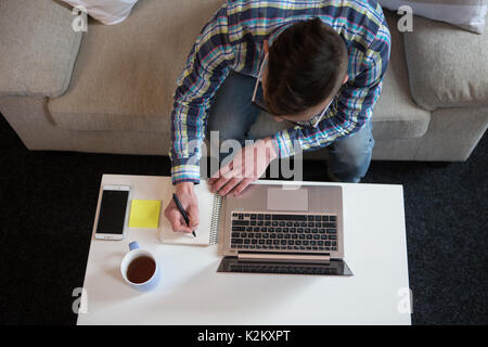 Freelancer homme travaillant à la maison, de prendre des notes en notebok. Le travail à distance à la maison, mâle qui fait travail à la maison. Banque D'Images