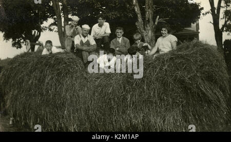 Meubles anciens c1930 photo, la famille et les amis jouent dans un gros tas de foin. SOURCE : photographie originale. Banque D'Images