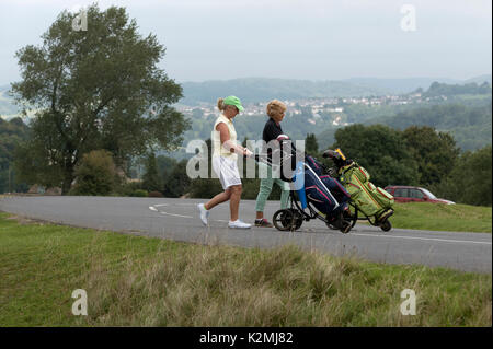 Dame golfeurs dans le sud de la région des Cotswolds England UK traversant une route de campagne avec leurs caddies de golf électriques. Auugust 2017 Banque D'Images