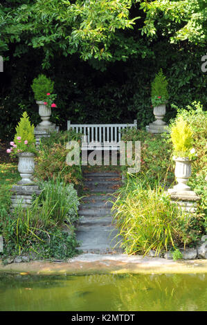 Un vieux banc de jardin dans un jardin paysager, au-dessus d'un escalier en pierre avec une sélection de plantes et fleurs quelque part pour s'asseoir dans le jardin Banque D'Images