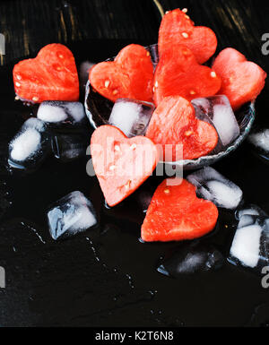 Watermelon coeurs avec des cubes de glace sur fond noir en noir pour la Saint-Valentin, selective focus, de l'espace pour le texte Banque D'Images