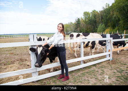 L'industrie de l'agriculture, de l'agriculture, les gens et l'élevage concept. jeune femme et les vaches en étable sur une ferme laitière. Banque D'Images