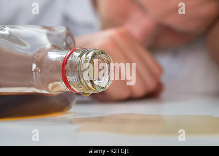 Jeune homme ivre dormir sur table avec une bouteille d'alcool Banque D'Images