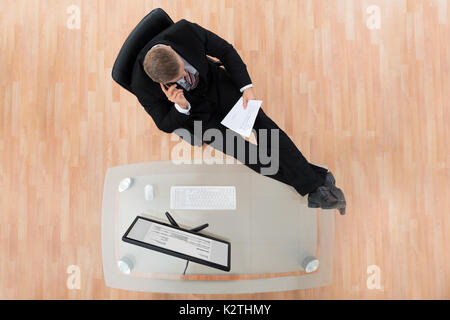 Businessman Reading Document tout en s'asseyant à la Desk In Office Banque D'Images