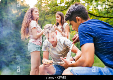 Les adolescents au camping, la cuisson des viandes sur le gril du barbecue. Banque D'Images