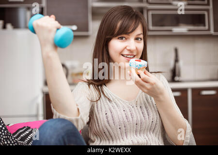 Young woman eating cupcake et holding hantel Banque D'Images