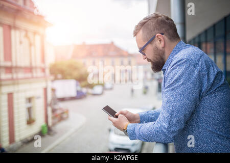 Homme debout au balcon et surfer sur le net sur smart phone Banque D'Images