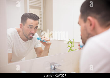 Reflet d'un homme séduisant se brosser les dents avec une brosse à dents électrique. Banque D'Images