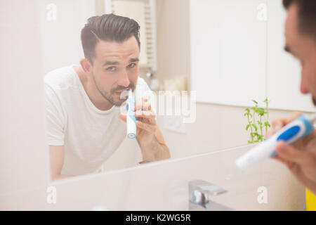 De joyeux dans la réflexion de miroir pendant le brossage des dents avec une brosse à dents électrique Banque D'Images