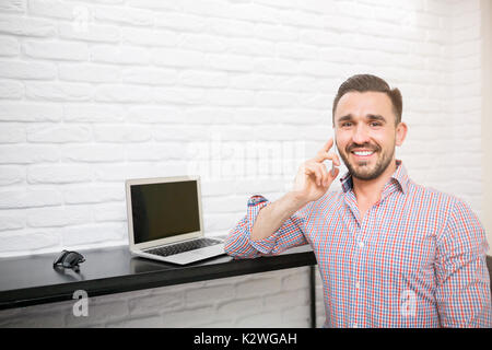 Homme assis dans la cuisine avec ordinateur portable et avoir une conversation agréable au téléphone Banque D'Images