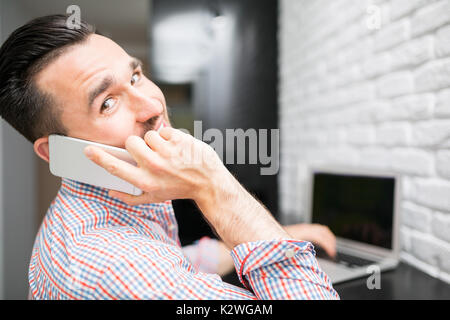 Homme heureux parler au téléphone dans la cuisine pendant que j'étais assis à table de cuisine avec coffre Banque D'Images