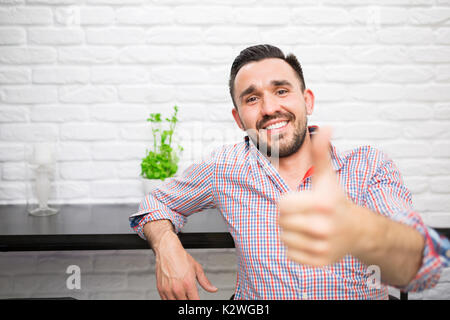 Cheerful young man showing bon geste alors qu'il était assis dans la cuisine Banque D'Images