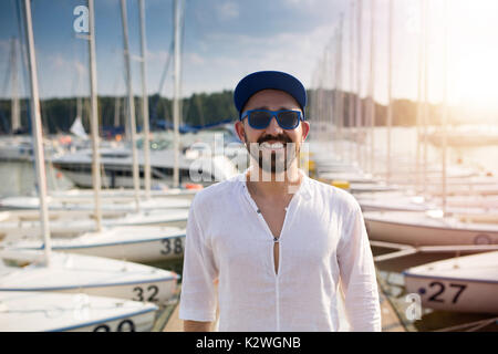 Young smiling man standing in voilier marina dans la lumière du soleil de l'après-midi Banque D'Images