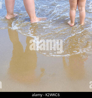 Mère et fille debout dans la plage tandis que quelques vagues en contact avec leurs pieds. Copie vide de l'espace pour l'éditeur de texte. Banque D'Images