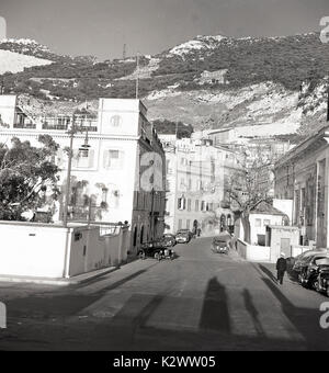 Années 1950, tableau historique du territoire britannique d'outre-mer de Gibraltar, montrant une ville rue avec des voitures en stationnement et la célèbre crête calcaire ou de rocher qui domine le paysage en arrière-plan. Banque D'Images