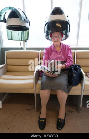 Personne âgée retraitée ayant ses cheveux séché dans un sèche-linge hotte portant des bigoudis dans un salon de coiffure dames, Angleterre, Royaume-Uni Banque D'Images