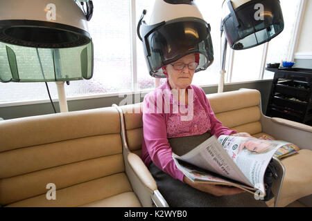 Personne âgée retraitée ayant ses cheveux séché dans un sèche-linge hotte portant des bigoudis dans un salon de coiffure dames, Angleterre, Royaume-Uni Banque D'Images