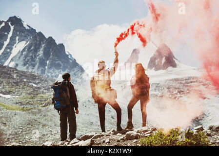 Groupe de trois amis avec flare rouge sur fond de montagnes Banque D'Images