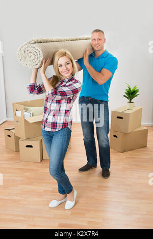 Happy Young Couple Carrying tapis roulé dans leur nouvelle maison Banque D'Images