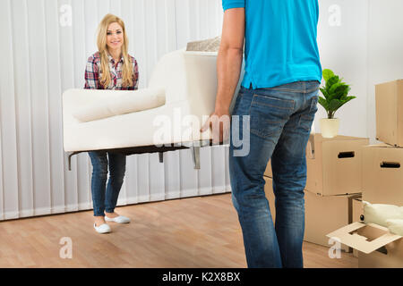 Happy Young Couple Carrying Sofa In New Home Banque D'Images