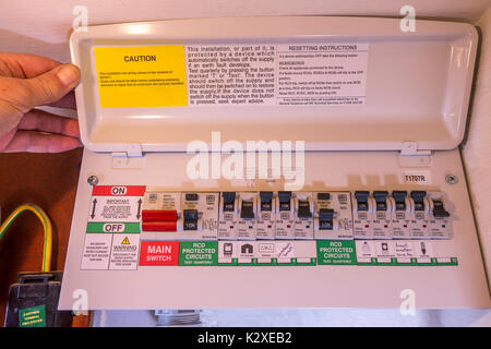 Le pouce et l'homme maintenant ouvrir le couvercle d'une unité de consommation d'électricité nouvellement montée, avec de multiples commutateurs on/off. Angleterre, Royaume-Uni. Banque D'Images