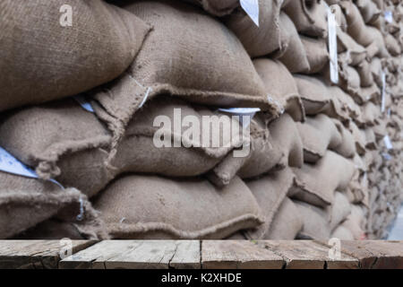 Vieux chanvre sacs contenant coffee bean en entrepôt. sacs empilés en entrepôt avec table en bois pour afficher votre produit. Banque D'Images