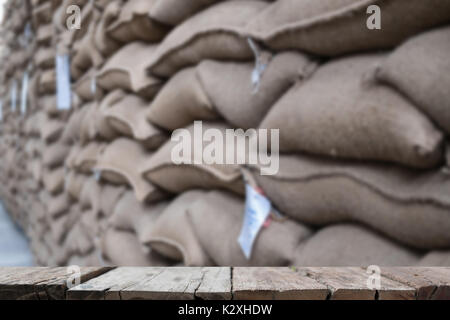 Vieux chanvre sacs contenant coffee bean en entrepôt. sacs empilés en entrepôt avec table en bois pour afficher votre produit. Banque D'Images