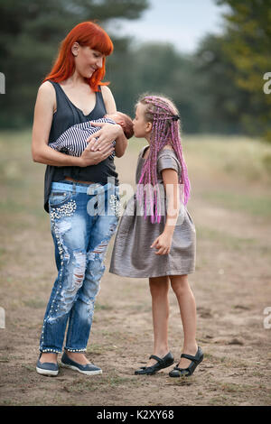 Mère heureuse avec ses deux enfants sur walk in park. Mère détient dans ses mains bébé nouveau-né, la fille se trouve à côté de mam et de baisers de son petit frère. Banque D'Images