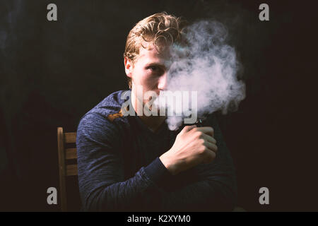 Jeune homme tenant isolé et une cigarette électronique ou vaping e cig sur un arrière-plan noir. Banque D'Images