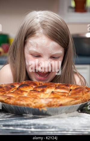 Une petite fille couverte dans la farine après la cuisson ou food fight rire et à plus d'une tarte aux pommes. Banque D'Images