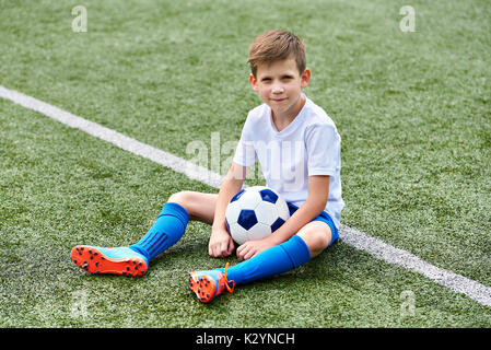 Garçon avec ballon de soccer de football assis sur une herbe verte Banque D'Images