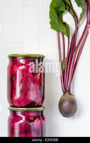 Deux pots en verre avec des betteraves en conserve et produits bio frais fait maison avec des betteraves fanes sur un fond en bois blanc Vue de dessus Banque D'Images