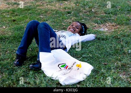 Une jeune fille souriant et portant dans l'herbe avec un sac en plastique au Baltimore Book Festival à Baltimore, Maryland, Septembre, 2013. Banque D'Images