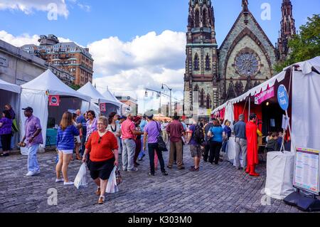 Une foule de personnes explorer vendeur tentes sur un chemin en brique avec une église avec vitraux en arrière-plan au Baltimore Book Festival, Baltimore, Maryland, Septembre, 2013. Banque D'Images