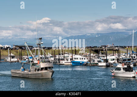 Un petit bateau de pêche revient de l'Kamishak Bay à la ville d'Homer et Port Harbour Marina surplombant les montagnes Kenai dans Homer, Alaska. Banque D'Images