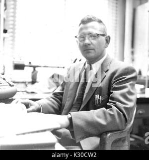 Francis Dewey Carlson, professeur de renommée internationale de biophysique à l'Université Johns Hopkins, est assis dans son bureau à son bureau, vêtu d'un costume et des lunettes, Baltimore, Maryland, 1959. Banque D'Images