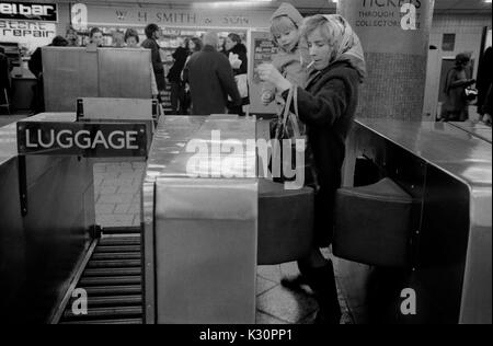 Métro station de métro nouveaux barrières de billets années 1970 mère et enfant, maman fume portant un petit enfant dans ses bras, 1975. HOMER SYKES, ROYAUME-UNI Banque D'Images