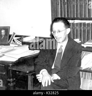 Portrait de Candide Nathan Edelman, Président du Département de Langues romanes à l'Université Johns Hopkins, assis à son bureau en face de bibliothèques, 1955. Banque D'Images