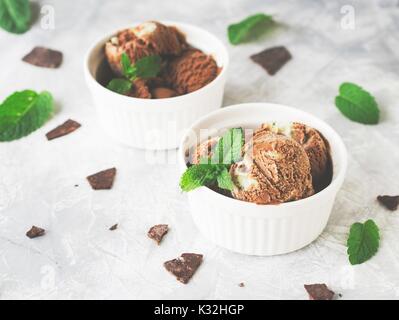 Glace à la menthe chocolat dans des bols blancs avec des morceaux de chocolat et de feuilles de menthe sur une table en marbre, selective focus, haute résolution Banque D'Images